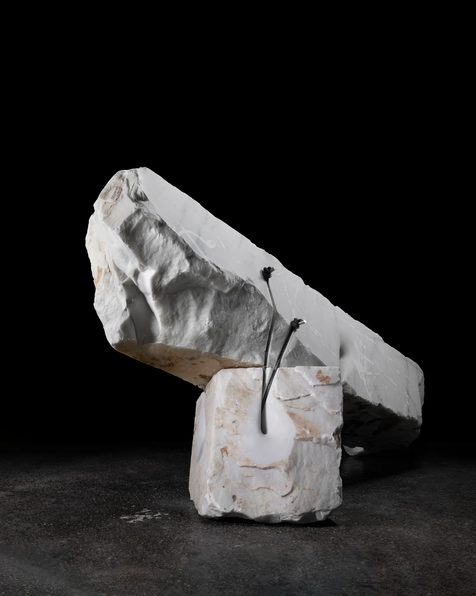White marble sculpture bound with steel cables against a dark background.