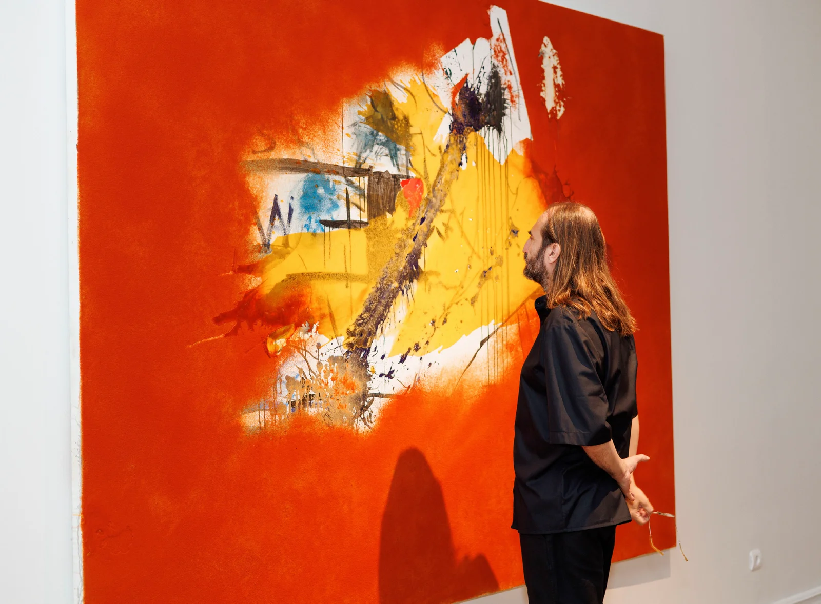 A visitor studies a large red painting with a yellow and black opening in Delicate Matter.